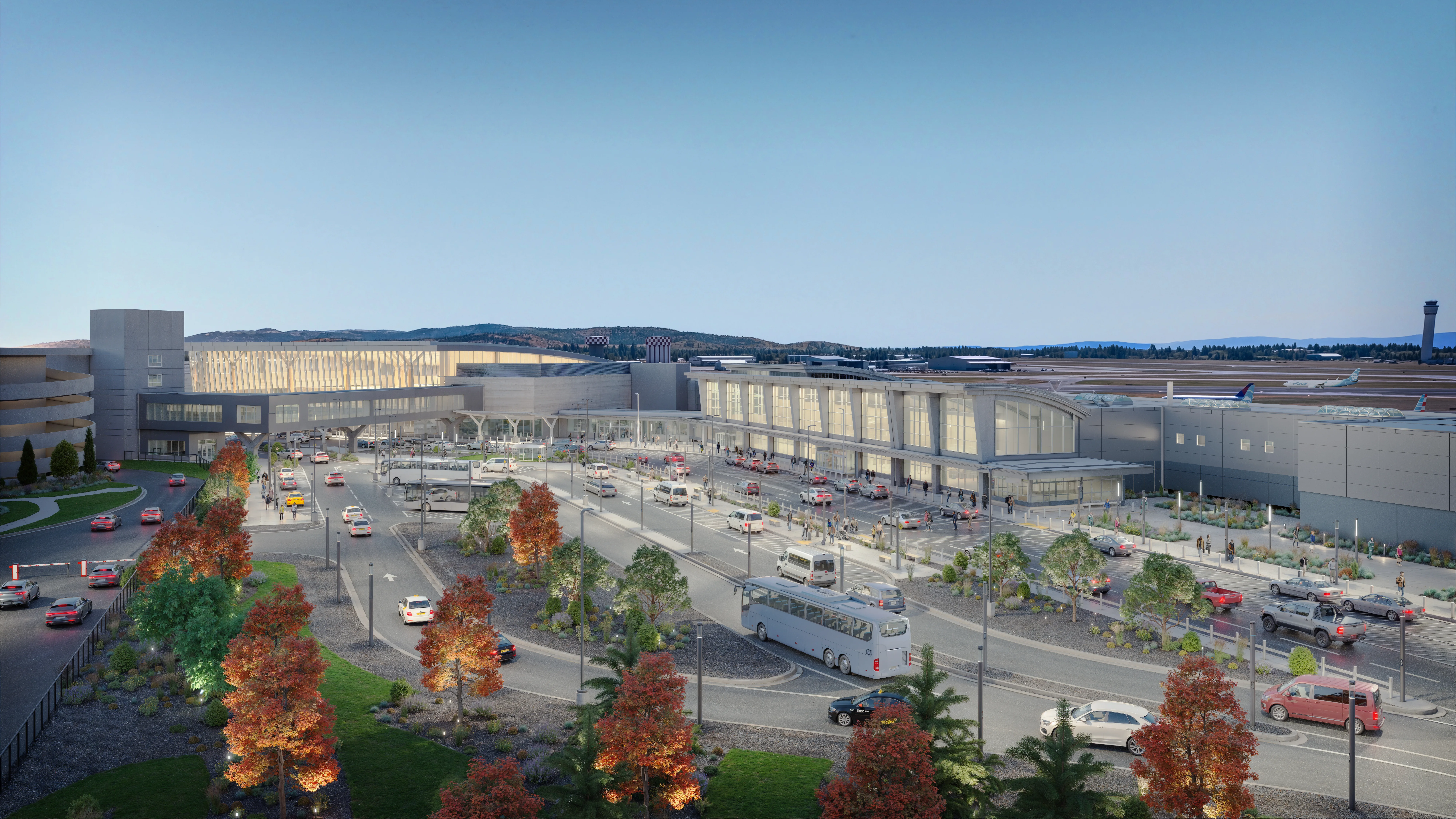 An aerial architectural rendering of the planned Spokane International Airport terminal expansion at dusk, showing a glowing glass-fronted terminal building, a multi-lane passenger drop-off roadway with vehicles and a bus, landscaped grounds with autumn trees, a parking structure, and the air traffic control tower visible in the distance.